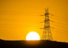 A sun on the horizon with electricity pylon and cables in the foreground