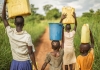 A group of young African children carry buckets of water on their heads.