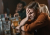man holding his head in pain while drinking at a public bar