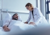 Man lying in bed while doctor checks his pulse