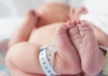 newborn baby in hospital bed lying on their back with hospital bracelets on feet
