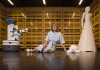 Mari Velonaki sits among robots in the Creative Robotics Lab