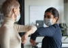 Two co-workers wearing masks and greeting each other in the office.
