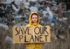 A child holding a poster on landfill with 'save our planet' written on it.