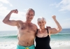 Smiling older couple flexing muscles at the beach