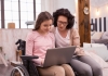 Teenage girl in wheelchair using a laptop next to her mother