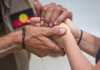 the hands of an indigenous man hold the hands of a young person