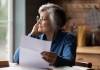 Thoughtful senior woman holding document smiles into the distance