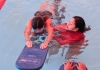 A swimming teacher with a student using a kickboard