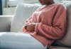 woman sitting on the couch and holding stomach