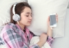 woman sleeping in bed while listening to music through headphones