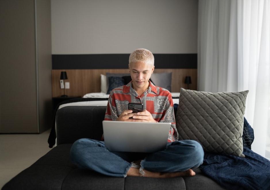 Man on laptop and smart phone in bedroom
